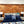 Bedroom with wooden wall paneling, bed with blue bedding and pillows, and nightstands with lamps.