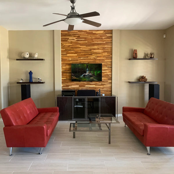 Modern living room with red couches, wooden wall, and ceiling fan.