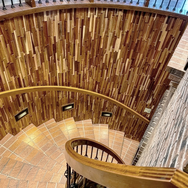 Spiral staircase with wooden handrails and tiled floor against a wooden paneled wall.