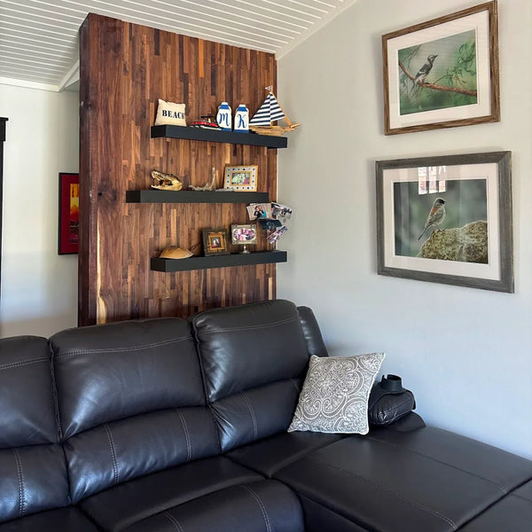 Living room with a black leather sofa, wooden wall panel with shelves, and framed pictures on the wall.