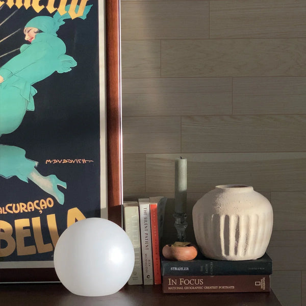 Decorative setup with books, a vase, and a spherical object against a wooden wall.