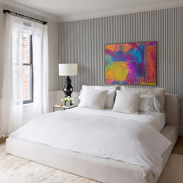 Modern bedroom with a bed, nightstand, lamp, and colorful abstract painting on the wall.