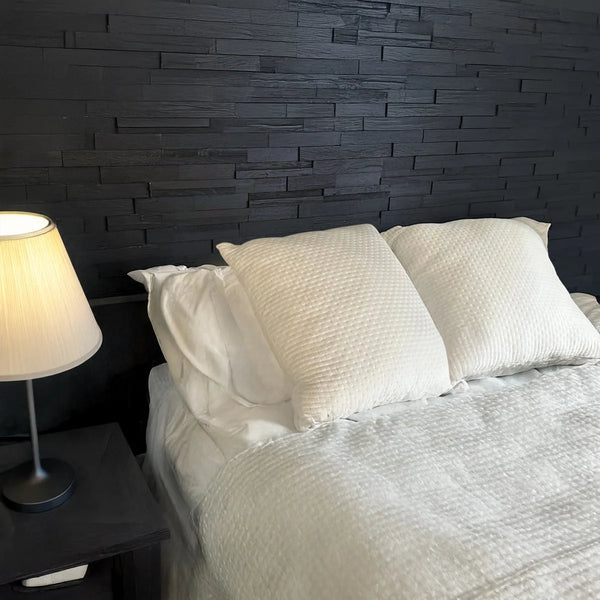 Bedroom with a bed, nightstand, and lamp against a dark brick wall.