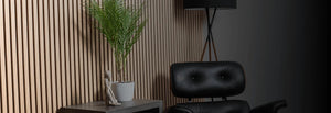 Modern interior with a black chair, plant, and lamp against a wooden paneled wall.