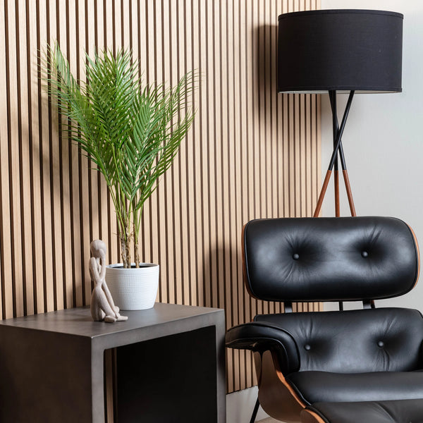 Modern interior with black leather chair, plant, and lamp against a wooden slat wall.